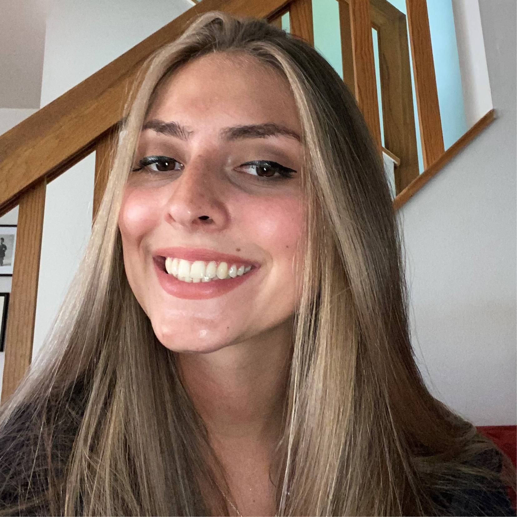 Image of a person smiling big while standing in front of a brick wall